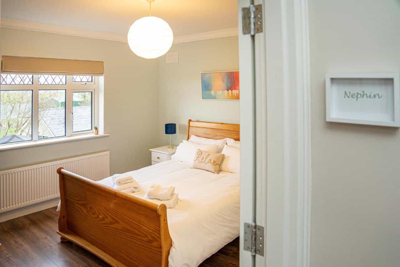 Bedroom with wooden sleigh bed, white linens, and framed "Nephin" sign visible through doorway.