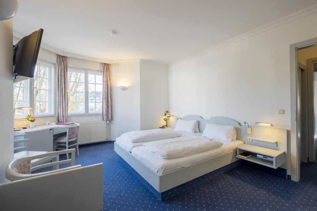 Hotel room with twin beds, desk, and view of trees outside windows near Woerthsee.