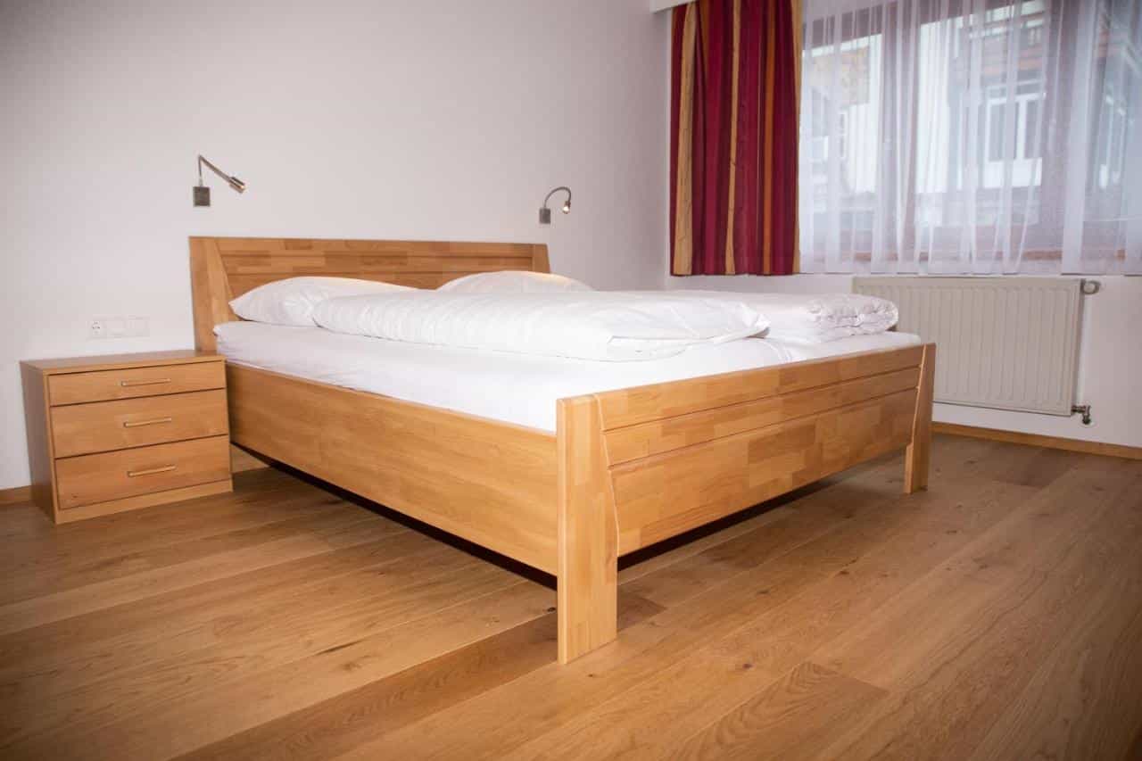 Wooden bed with white linens, nightstand, and wood floor in St. Johann room.