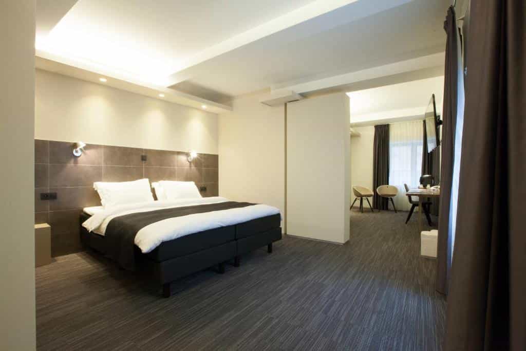 Modern hotel room with large bed, dark carpet, and separate seating area visible through doorway.