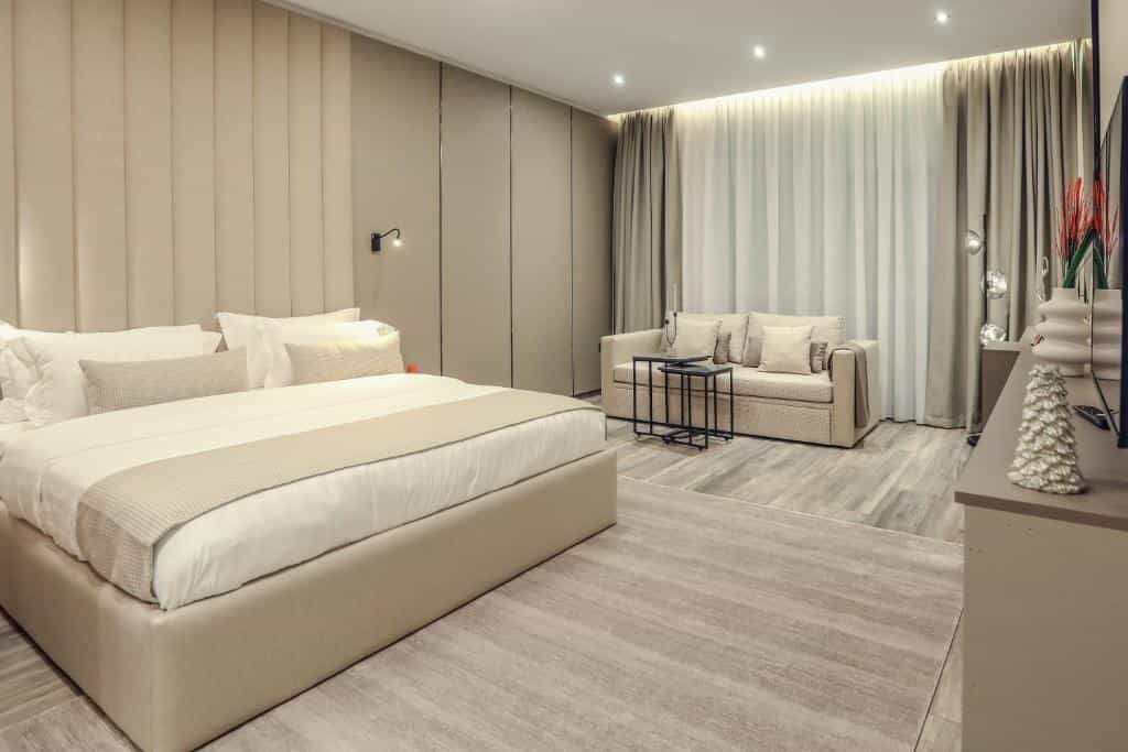 Modern hotel room with beige upholstered bed, sofa, and light wood-look flooring in Hotel Dirista Shkoder.