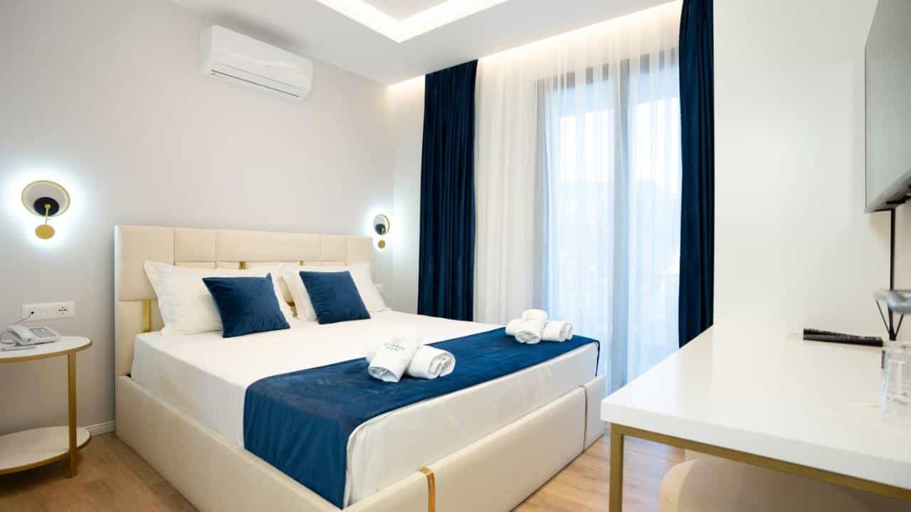 Modern hotel room with beige bed, blue accents, and white sheer curtains in Vlore.