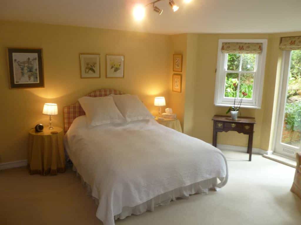 Bedroom with yellow walls, white bedding, and a window showing greenery outside