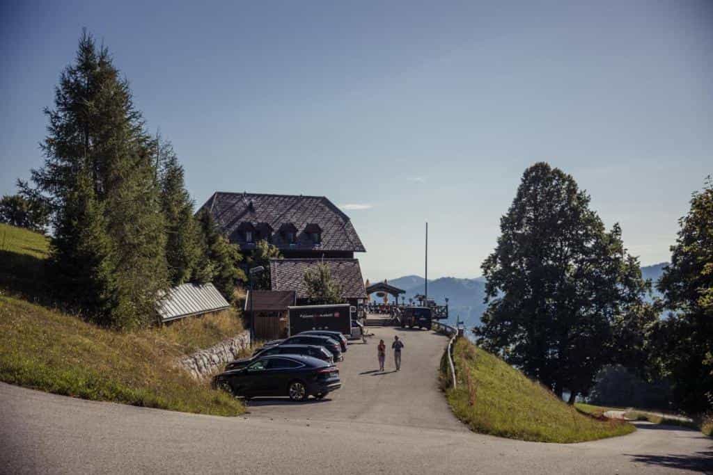 Gmundnerberghaus building with parking lot, people walking, and mountain view.
