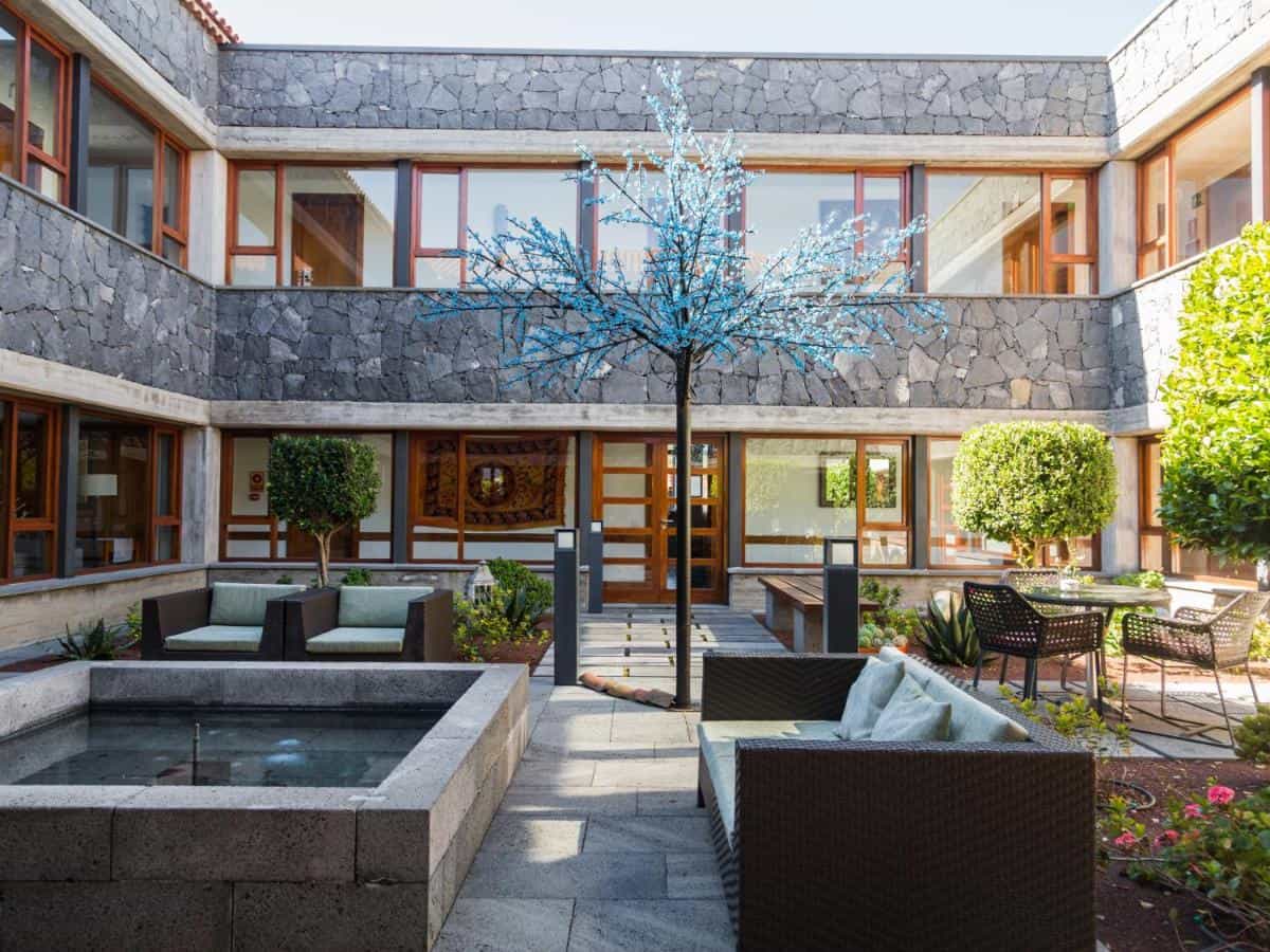 Courtyard patio of La Casona del Patio with stone walls, blue tree, and outdoor seating.