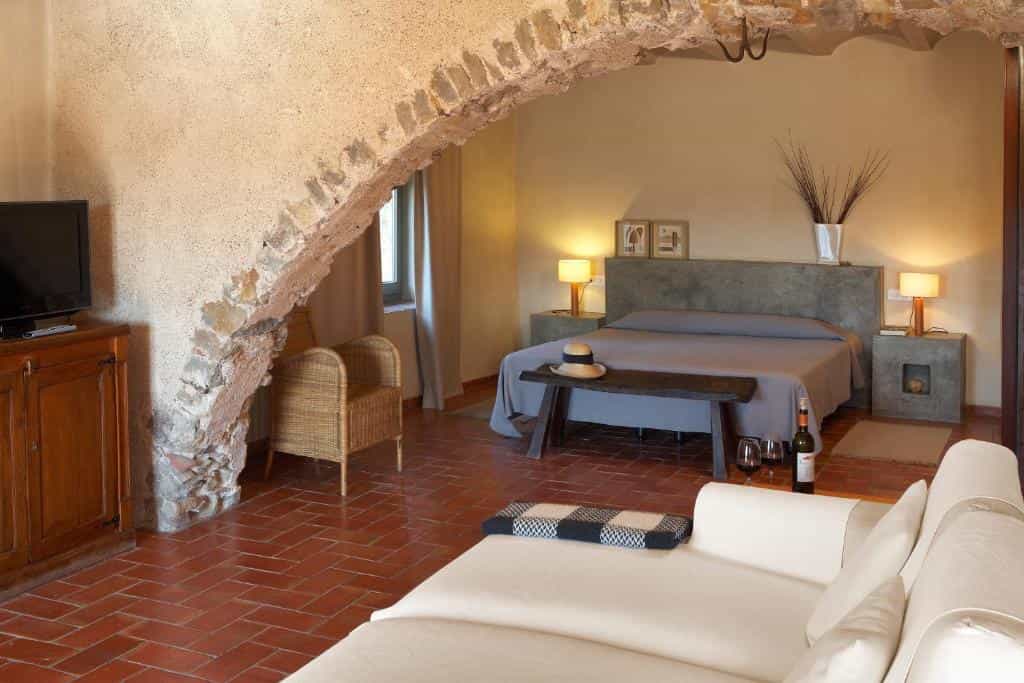 Hotel room with stone archway, terracotta floor, bed, and seating area.