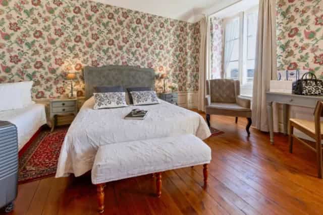 Hotel bedroom with floral wallpaper, double bed, armchair, and wooden floors.