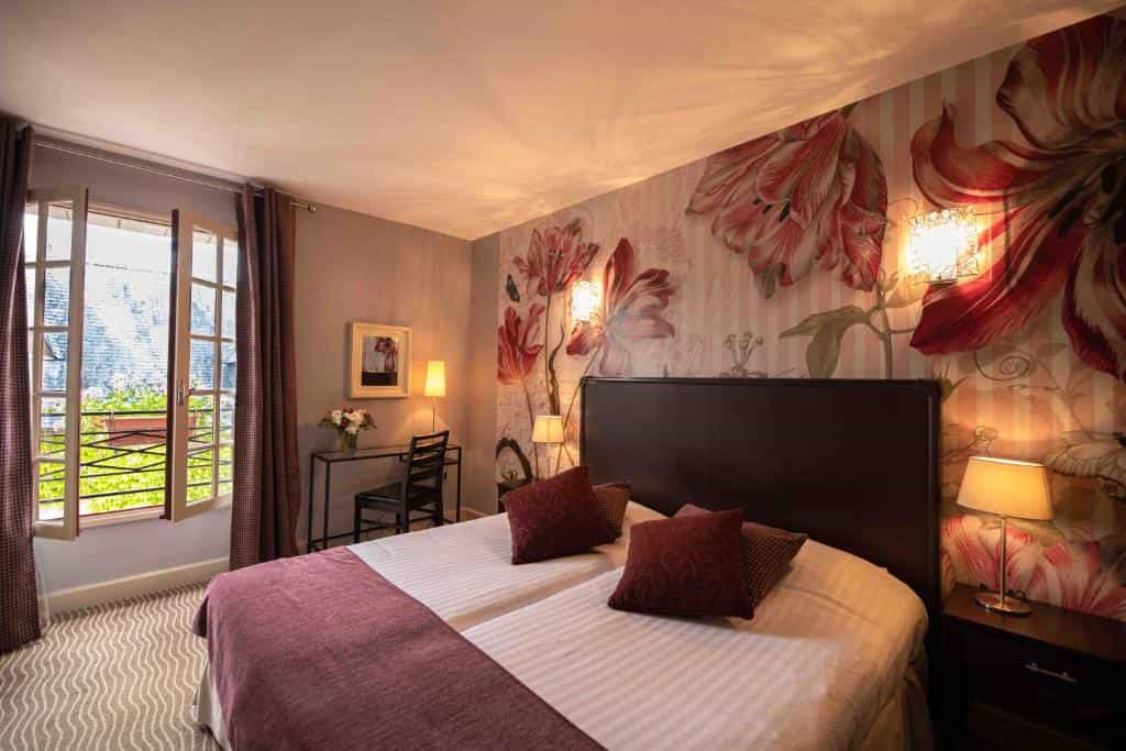 Hotel bedroom with double bed, floral wallpaper, and open window overlooking a street.