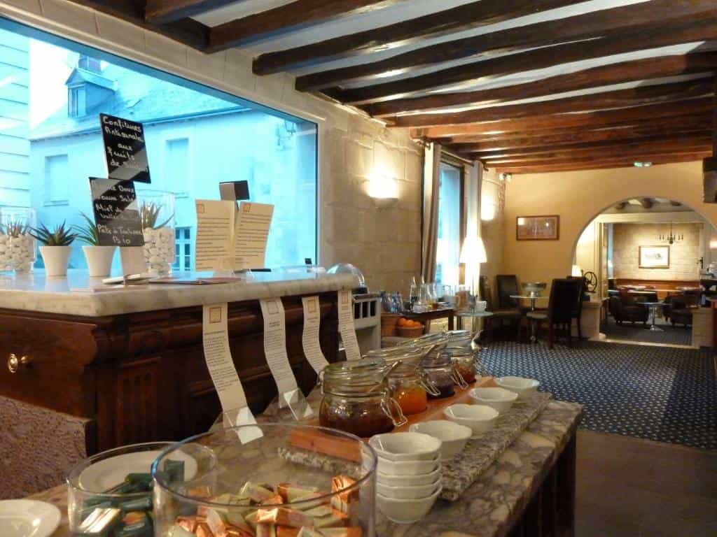 Breakfast buffet area with jars of jam and condiments in a rustic hotel interior with stone walls and wooden beams.