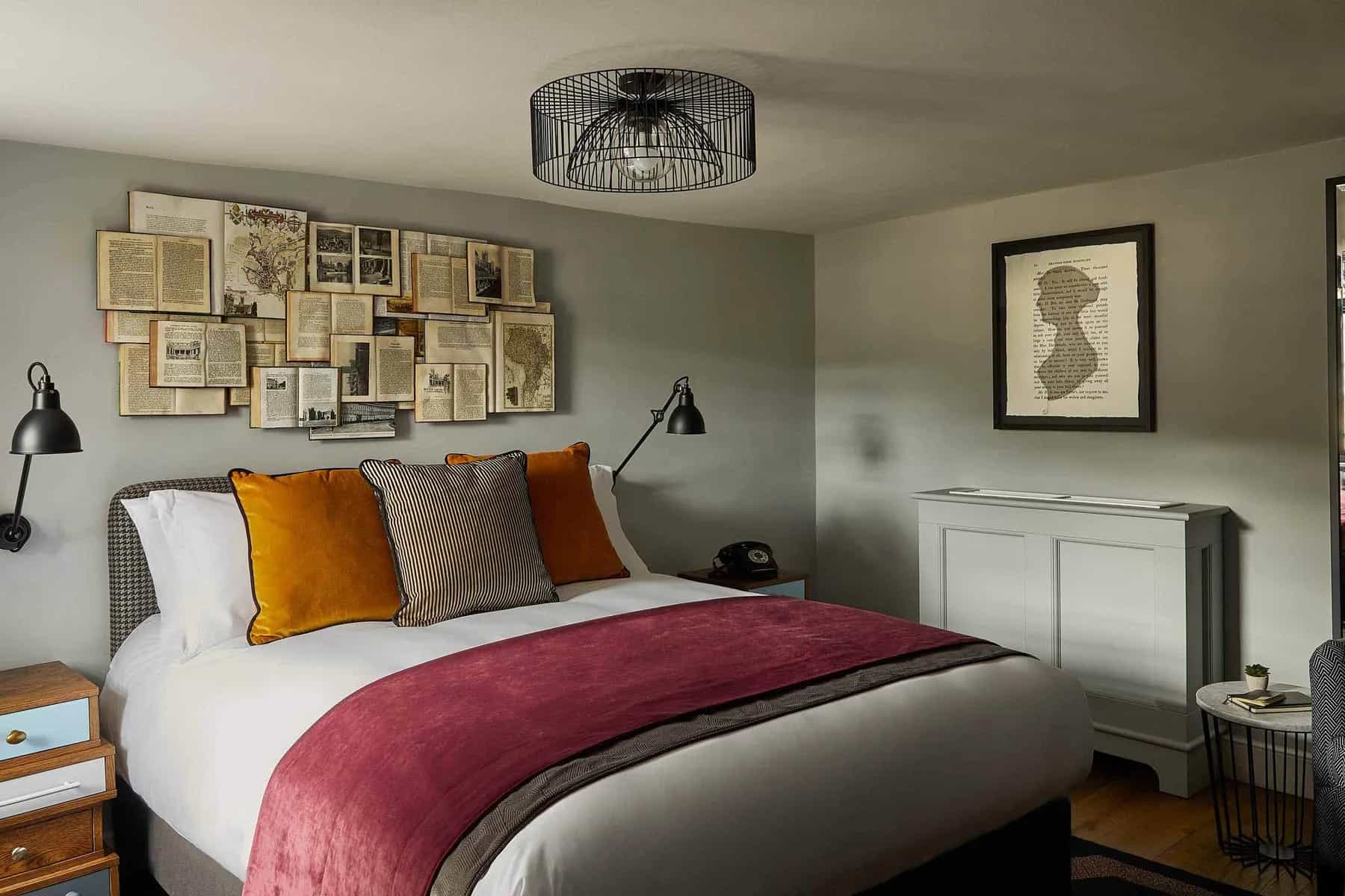 Hotel bedroom with a double bed, mustard and striped pillows, and a wall display of vintage book pages.