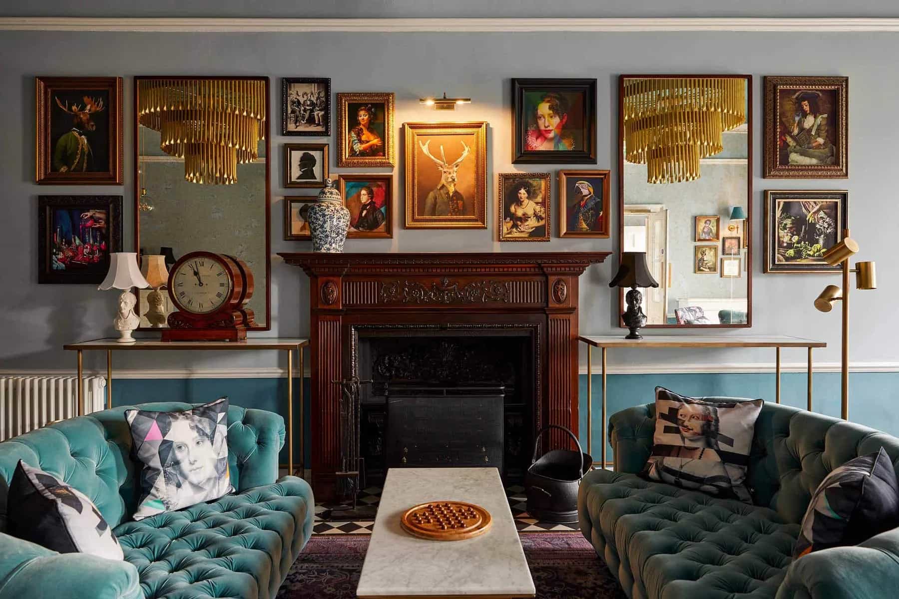 Living room with teal tufted sofas, wooden fireplace, gallery wall of framed portraits, and two large mirrors.
