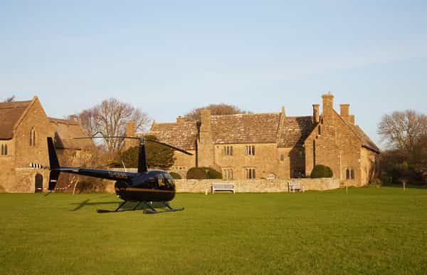 Black helicopter parked on a green lawn in front of a historic stone manor house.