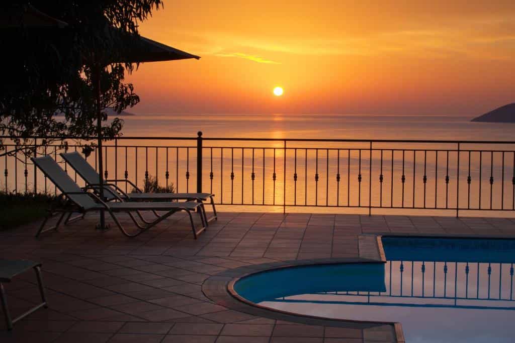 Sun loungers on a tiled pool terrace overlooking the sea at sunset.