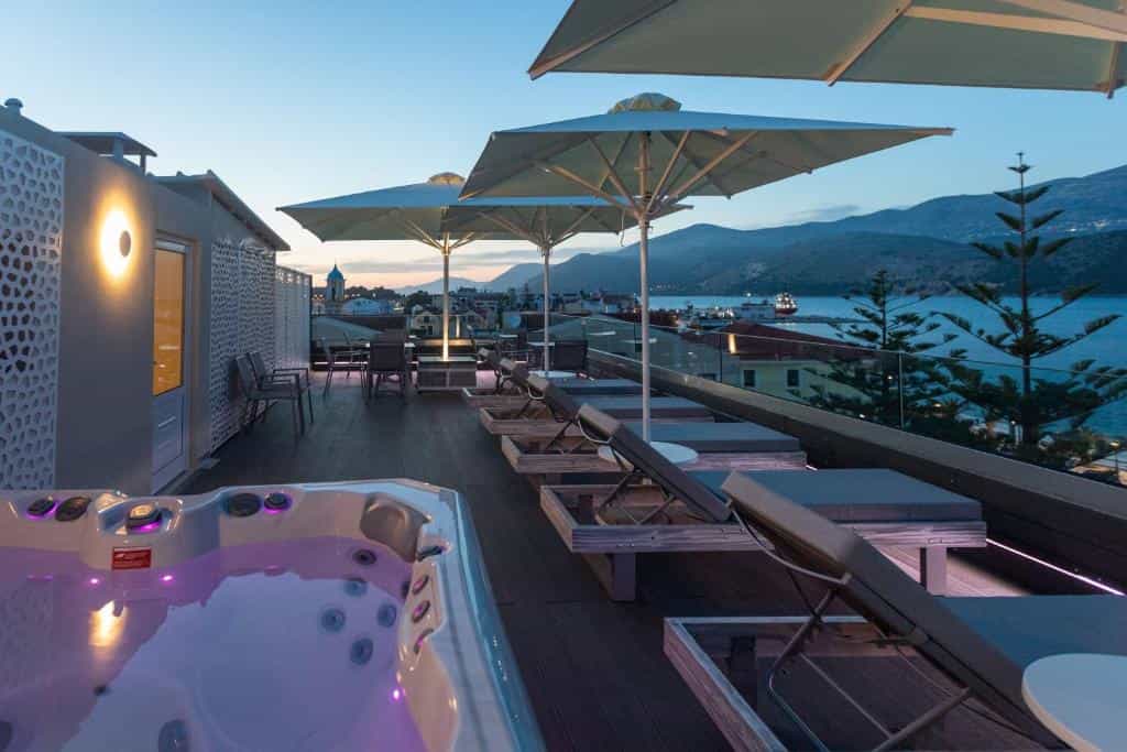 Rooftop terrace with hot tub, sun loungers, and umbrellas overlooking a coastal town and harbor at dusk.