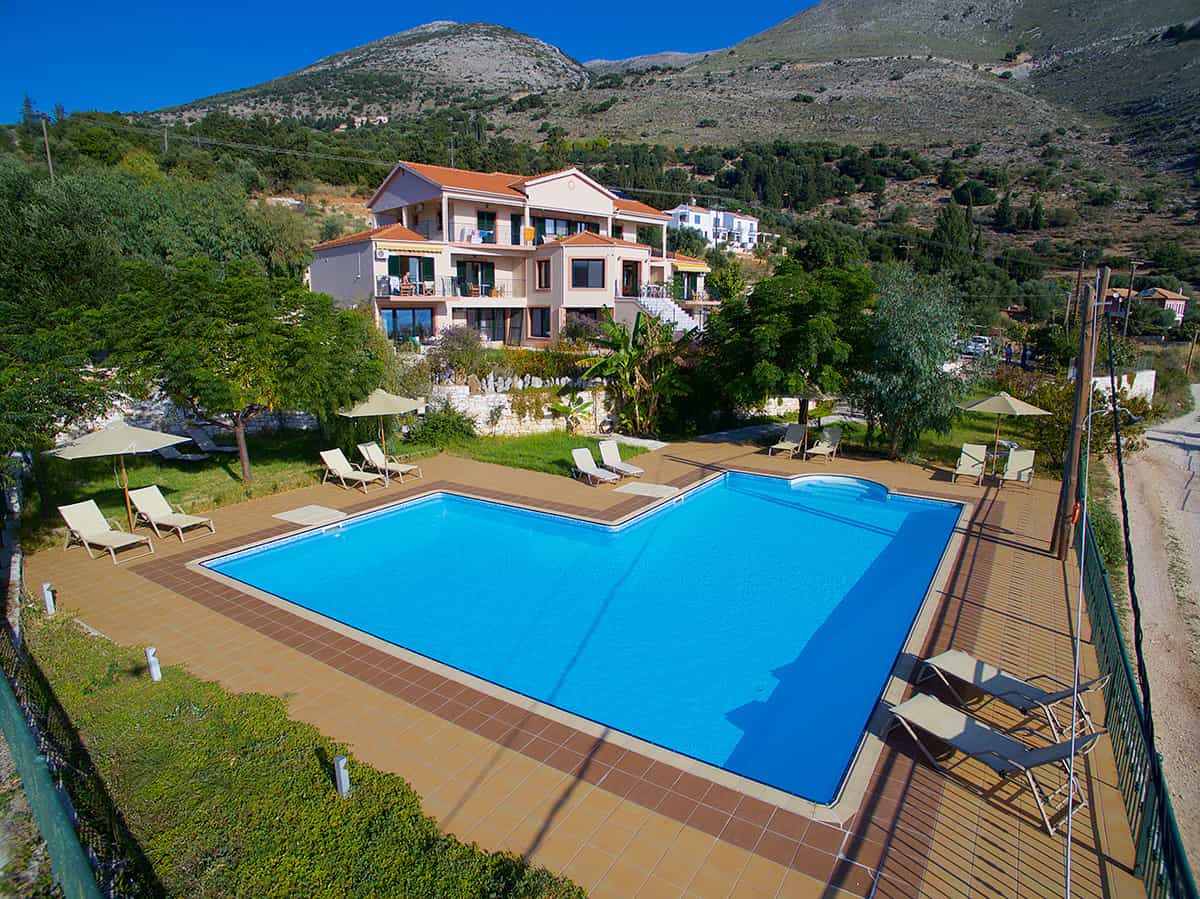 Swimming pool with sun loungers and umbrellas at a hotel in Agia Efimia, Kefalonia, set against a mountain backdrop.
