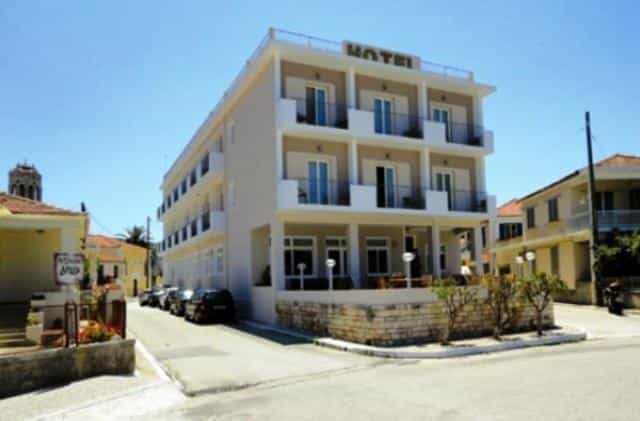Three-story hotel building with balconies on a street in a Mediterranean-style town.