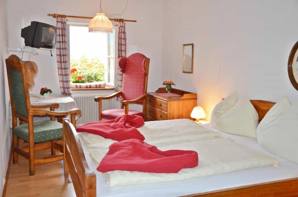 Cozy bedroom with wooden furniture, red accents, and an open window overlooking flowers.