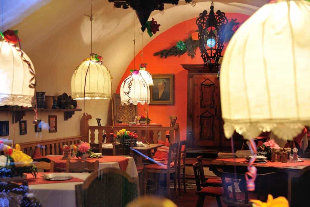 Cozy restaurant interior with warm lighting, wooden furniture, and red tablecloths.
