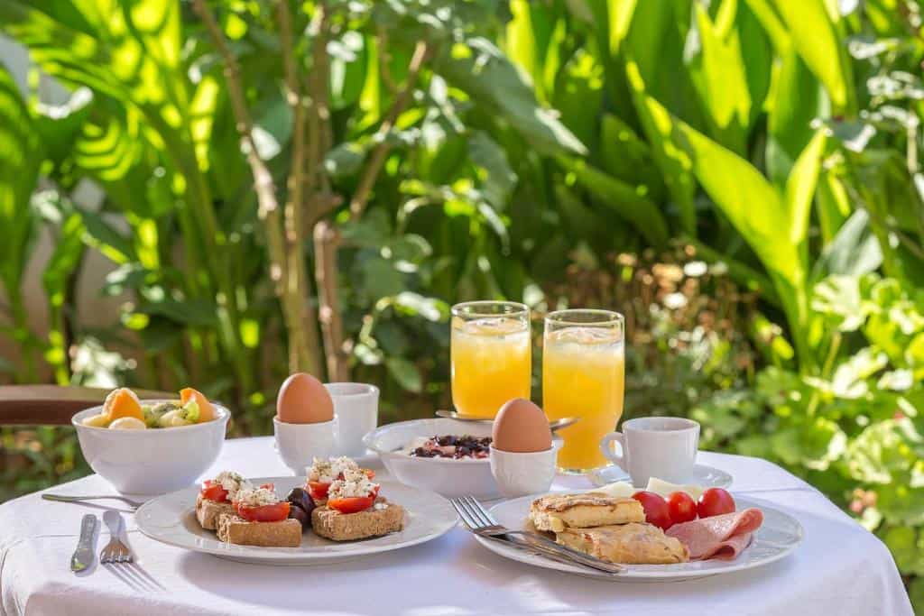 Breakfast spread with eggs, fruit, and juice on a table outdoors in a garden setting.
