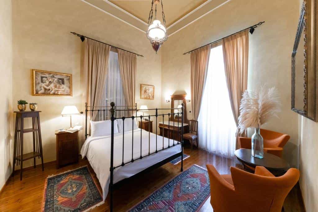 Hotel bedroom with wrought iron bed, wooden floors, and orange armchairs.