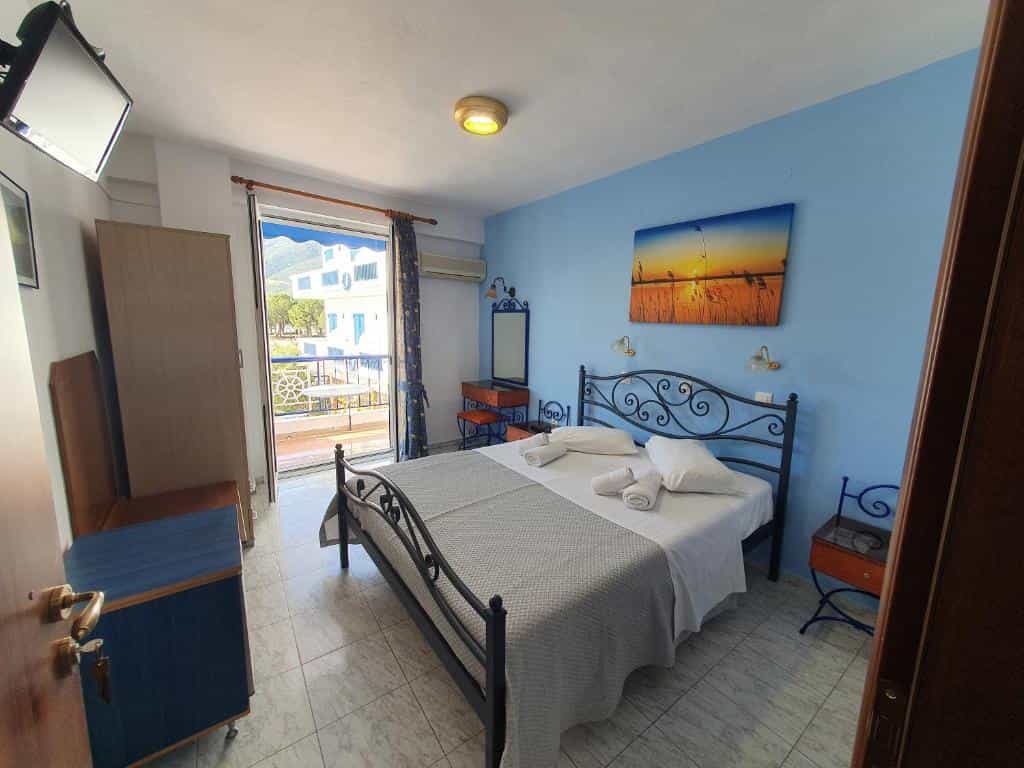 Hotel room with double bed, blue walls, and balcony overlooking a sunny outdoor area.