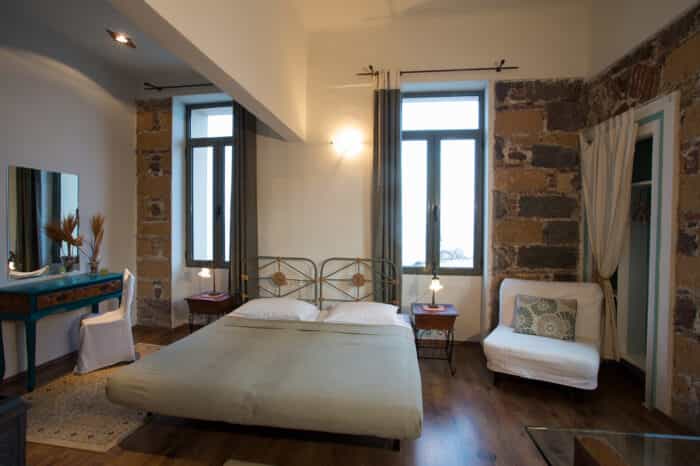 Hotel room with double bed, exposed stone walls, and wooden floors.