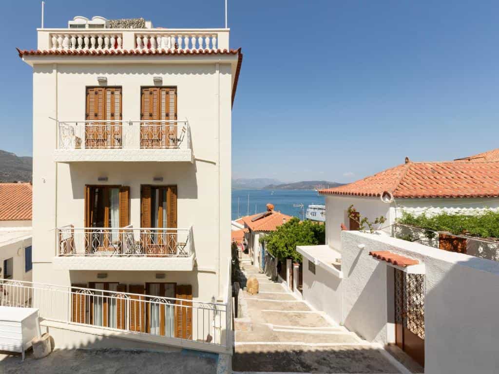 White building with balconies overlooking a coastal village street and the sea.
