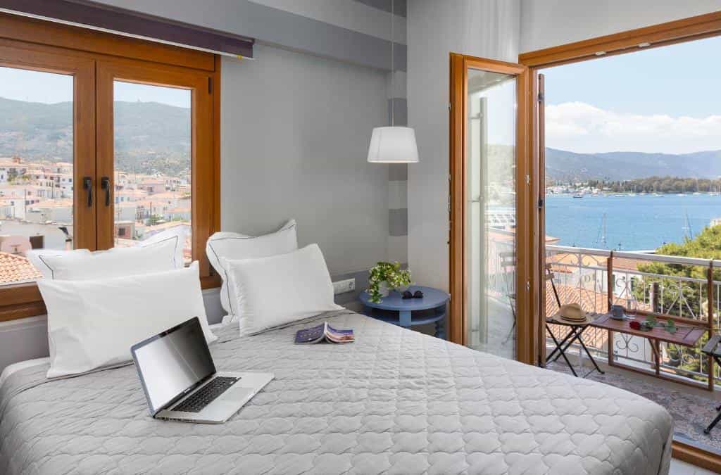 Hotel room with laptop on bed and balcony overlooking coastal town and sea.