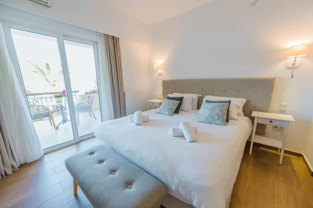 Hotel room with a double bed, bench, and sliding glass door leading to a balcony.