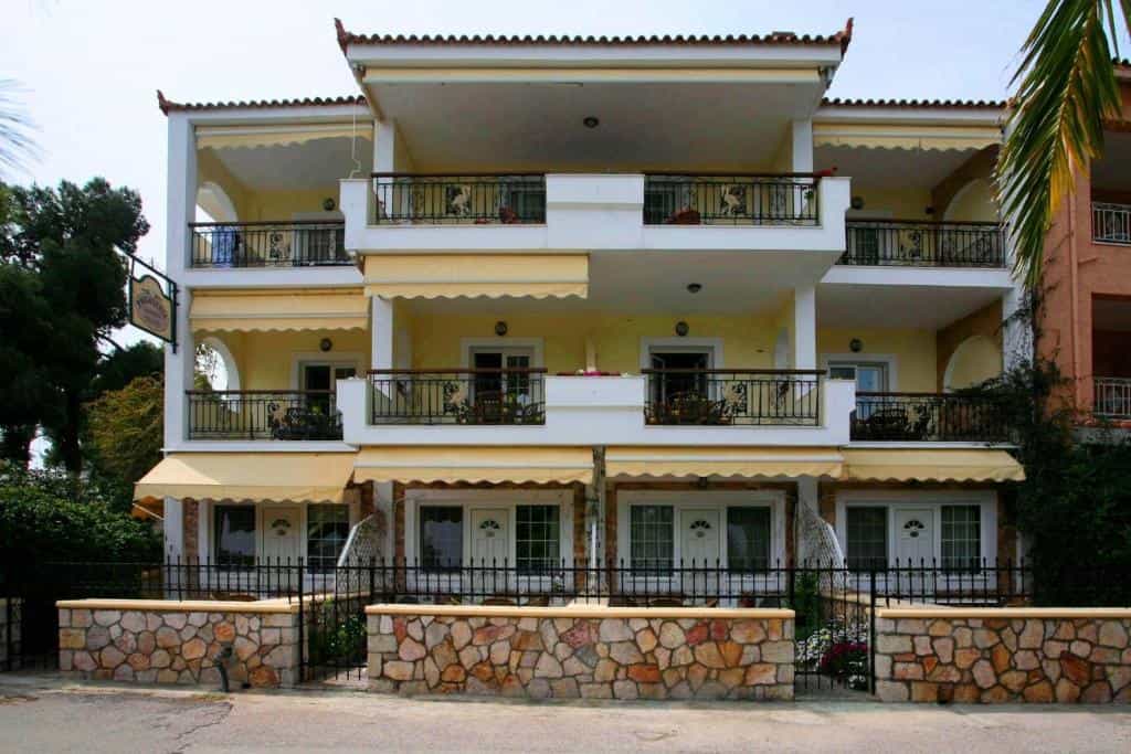 Three-story apartment building with balconies, yellow awnings, and a stone wall fence.