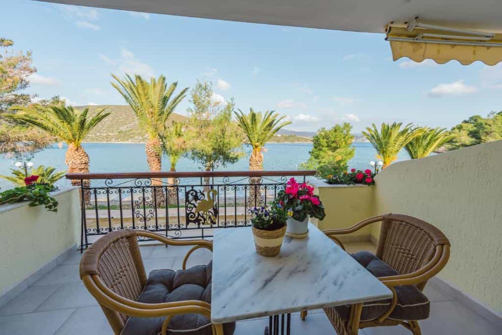 Balcony with marble table and wicker chairs overlooking a coastal sea view with palm trees.