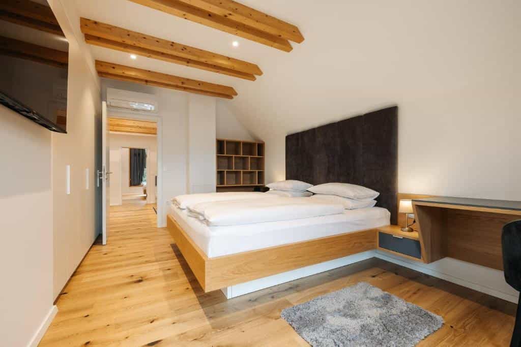 Modern hotel bedroom with wooden ceiling beams, hardwood floors, and a queen bed in Bled, Slovenia.