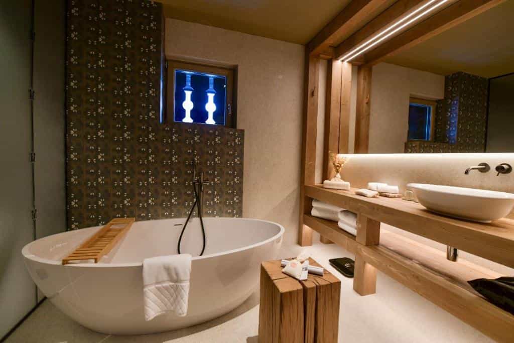 Modern bathroom with a freestanding white bathtub, wooden vanity, and patterned tile wall.