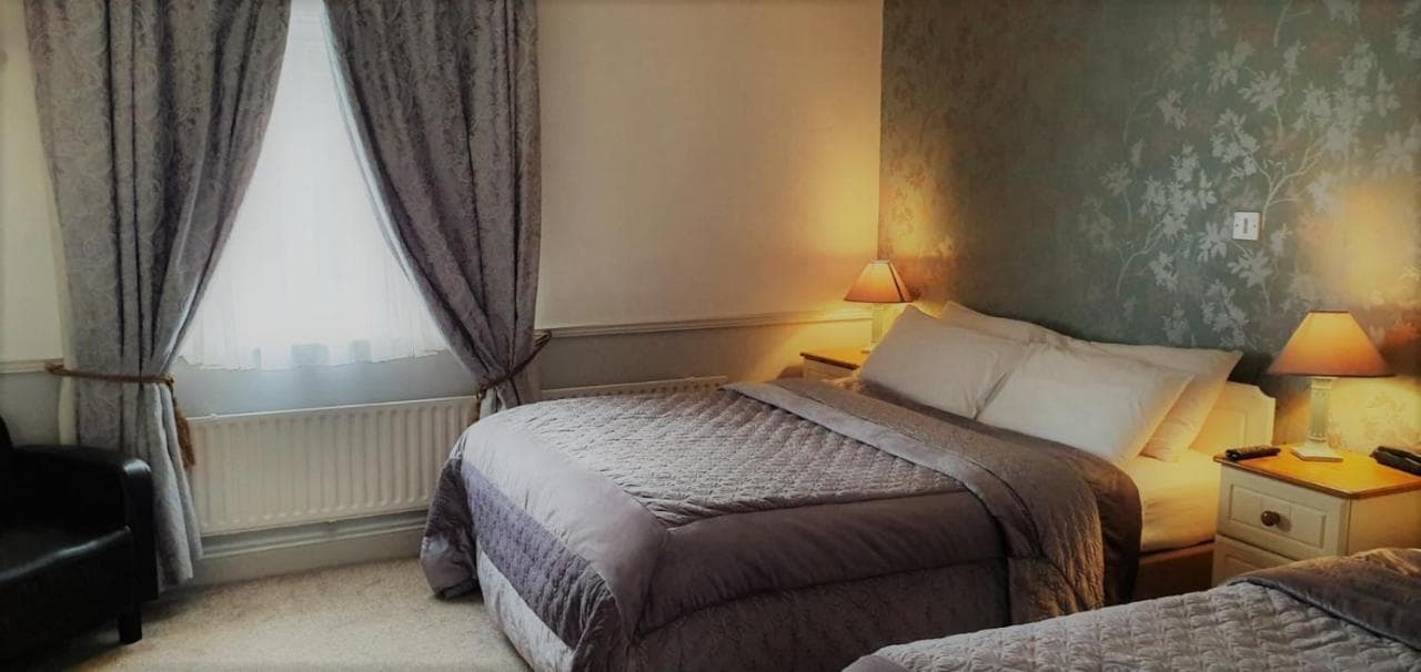 Bedroom in Danagher's Hotel with two beds, patterned wallpaper, and heavy curtains.
