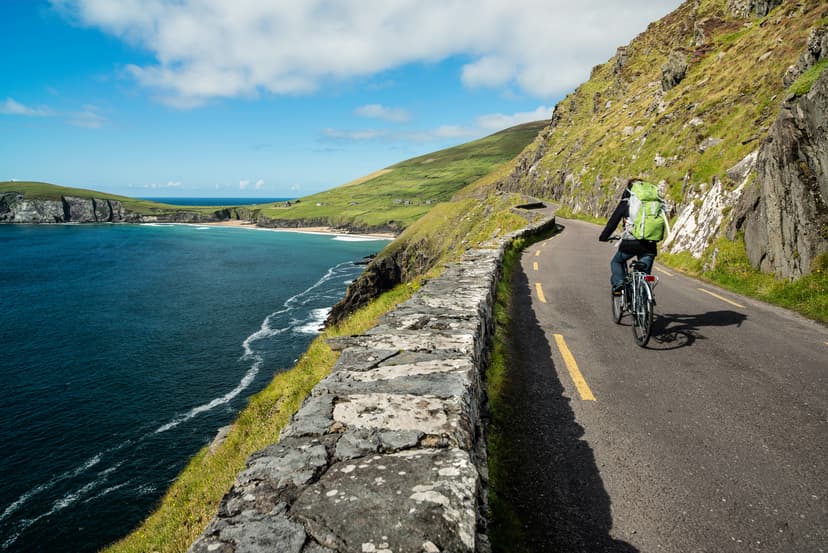 Cyclist on winding coastal road above dark blue sea in Ireland.