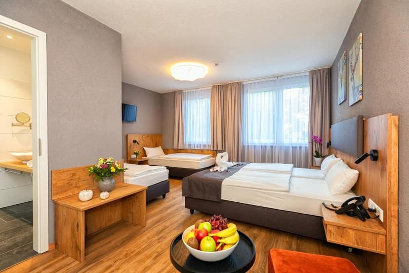 Triple hotel room with wooden floors, multiple beds, and a view of the bathroom.