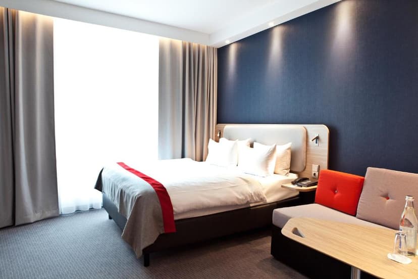 Modern hotel room with bright window, white bedding, and dark blue accent wall in Trier