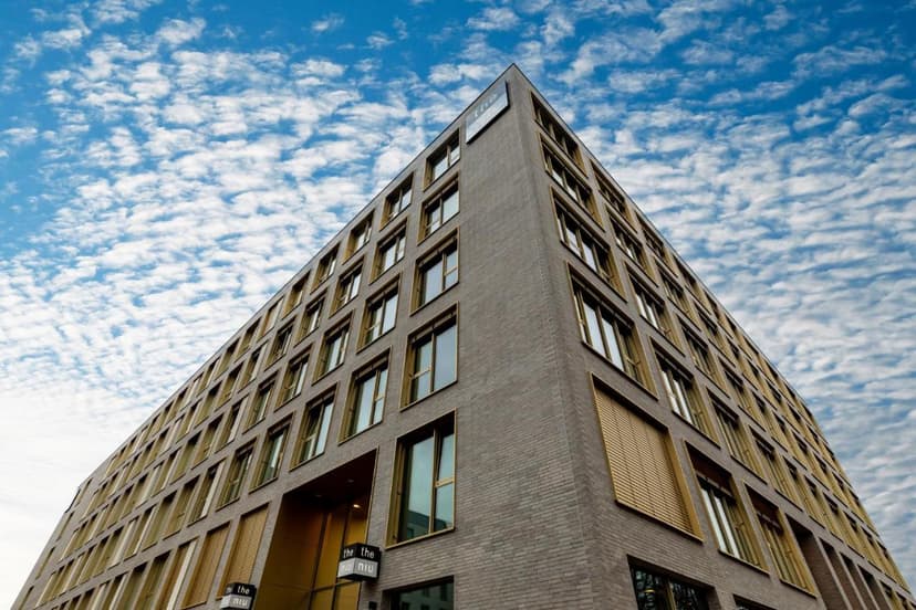 Modern hotel building exterior with gray brick and gold window frames under a cloudy blue sky in Konstanz.