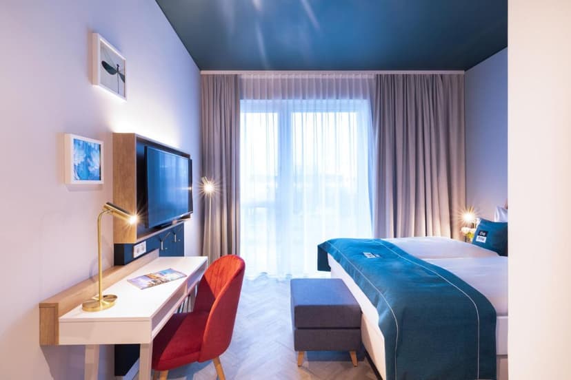 Hotel room interior with bed, desk, red chair, and bright window in Konstanz Holiday Inn.