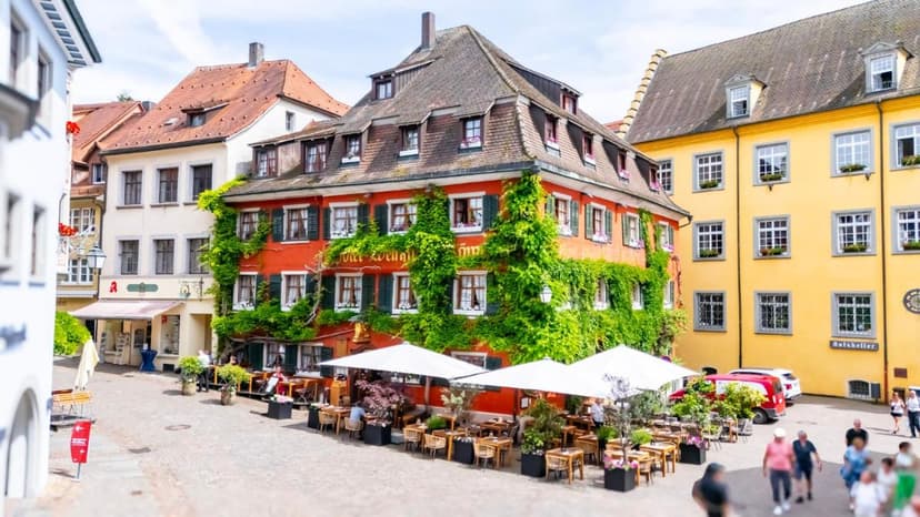 Outdoor dining at Hotel Löwen Weinstube in Meersburg with ivy-covered red building.