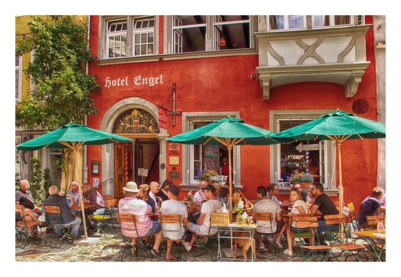 Outdoor dining at Hotel Engel with green umbrellas on a cobblestone street in Lindau.
