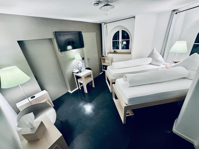 Twin beds in a modern room with a wall-mounted TV and arched window at Bed-Bike-and-Breakfast Olten.