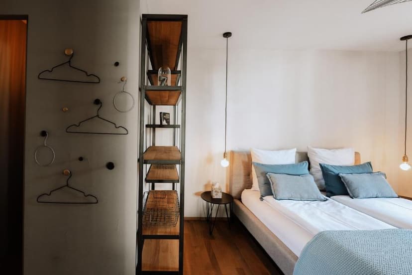 Bedroom with twin beds, modern shelving unit, and wire hangers on a gray wall in Murten.