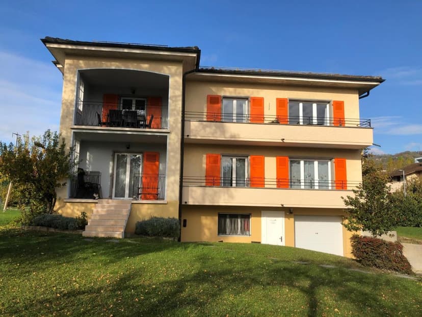 Yellow apartment building with orange shutters and green lawn in Lausanne, Au Bonheur des Iris.