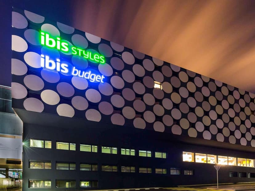 Ibis Styles and Ibis Budget hotel exterior at night with illuminated signs and polka-dot facade in Geneva.
