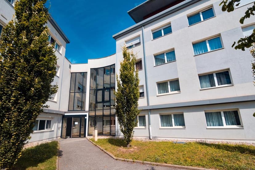 Modern hotel residence exterior in Annecy with glass entrance and trees under blue sky.