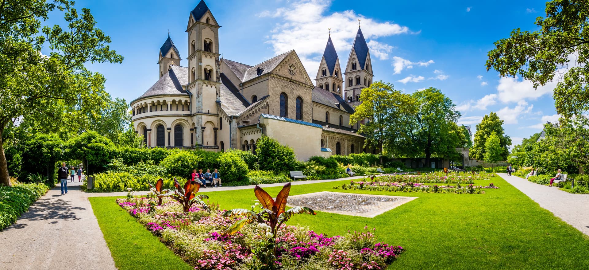 Koblenz Cathedral viewed from a sunny park with flower beds and green lawns.