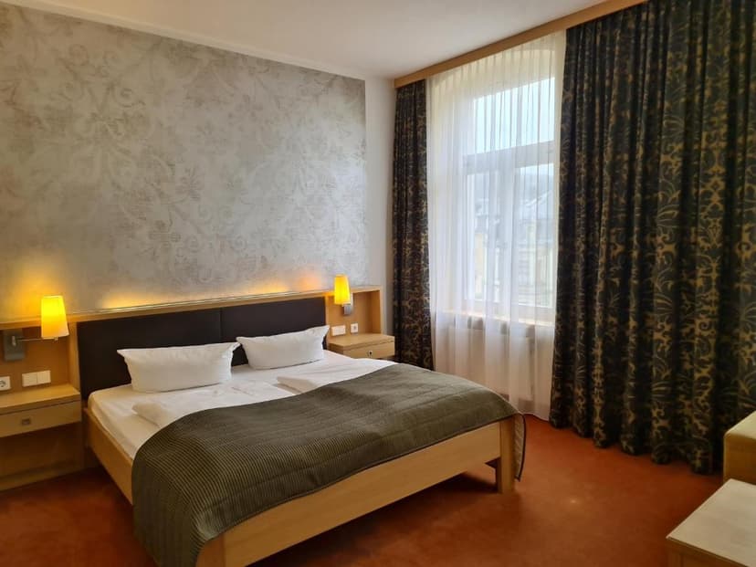 Hotel room with wooden bed, patterned wallpaper, and dark patterned curtains in Bad Schandau.