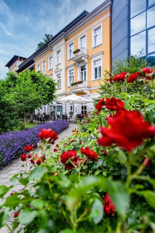 Hotel exterior with yellow facade, garden path, red roses, and purple lavender in Bad Schandau.