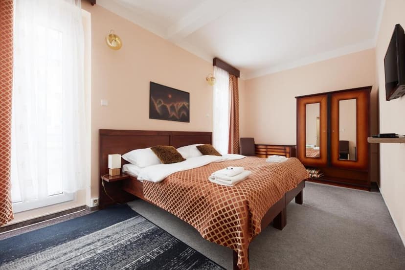 Hotel room with wooden bed, patterned brown spread, and mirrored wardrobe in Litomerice